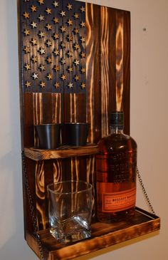 a bottle of whiskey and two shot glasses on a wooden shelf with an american flag