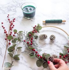 someone is making a wreath out of pine cones and red berries on a marble table