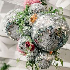 a bunch of disco balls hanging from a ceiling with flowers and greenery around them