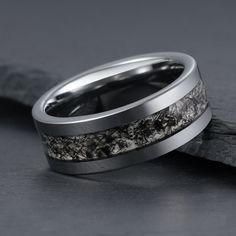 a wedding band with white gold and black diamond inlays, set on top of a piece of wood