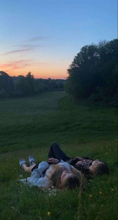 two people laying in the grass with their arms around each other as the sun sets