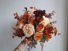 a woman holding a bouquet of flowers in her hand with leaves and foliage around it