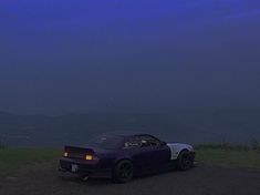 a purple sports car parked on top of a hill in the dark night with mountains in the background