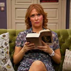 a woman sitting on a green couch holding a book in her hands and looking at the camera