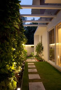 an outdoor garden with grass and lights on the side of it, next to a house