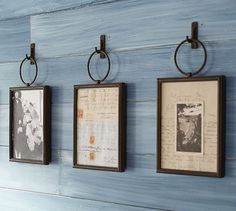 three framed pictures hang on a blue wall with metal rings hanging from it's sides