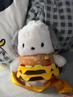 a stuffed animal with a hamburger in it's mouth sitting on a bed next to pillows