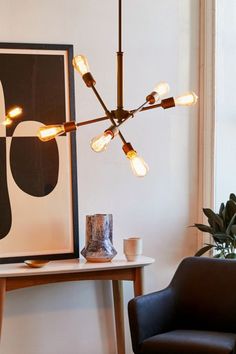 a modern chandelier hangs over a small table with a chair and potted plant