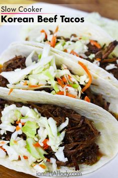 three shredded beef tacos with cole slaw and carrots on top, sitting on a white plate