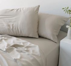 a bed with white sheets and pillows on top of it next to a vase with flowers