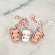 three pink and white cups with the words team bride to be written on them sitting next to beads