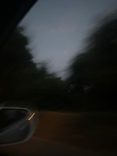 blurry photograph of trees and sky taken from inside a car window at night time