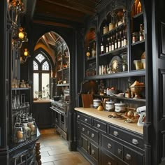 an old fashioned kitchen with black cabinets and wood flooring on the walls, along with lots of glassware