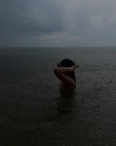 a woman is standing in the water with her arms around her head looking out to sea