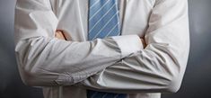 a man wearing a white shirt and blue tie with his arms crossed in front of him