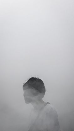 a man is standing in the fog with his head turned to the side and looking at something