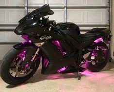 a black motorcycle parked in front of a garage door with purple lights on it's side