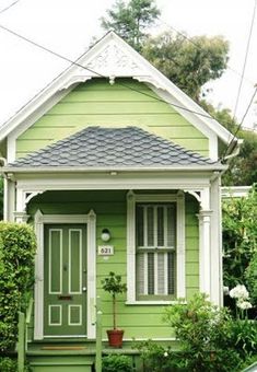 a green house with white trim on the front door and windows, next to some shrubbery