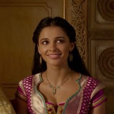 a woman in a pink and gold sari is smiling at the camera with her hand on her hip