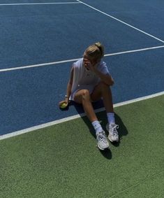 a woman sitting on the tennis court holding a tennis ball