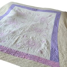 a purple and white quilt on top of a bed next to a pillow cover with flowers