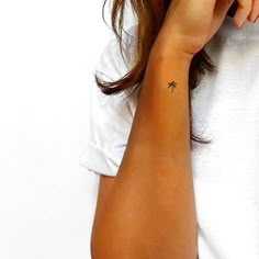 a woman with a small palm tree tattoo on her left arm and right hand behind her ear