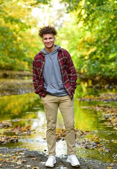 a young man standing in the middle of a stream with his hands in his pockets