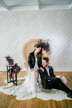 a bride and groom sitting on a chair in front of a white wall with flowers