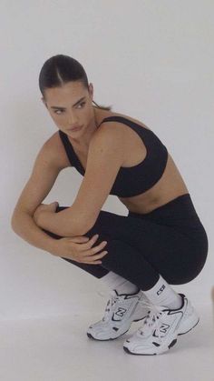 a woman squatting on the ground with her hands behind her back and legs crossed