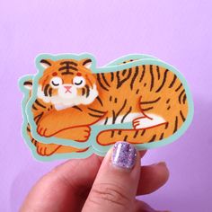 a hand holding up a sticker with a tiger on it's face and glitter nail polish