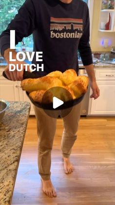 a man standing in a kitchen holding a pan filled with food