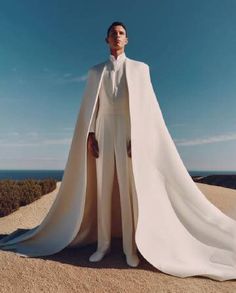 a man in a white suit and cape standing on top of a hill