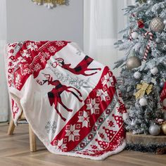 a red and white christmas blanket sitting on top of a wooden floor next to a tree