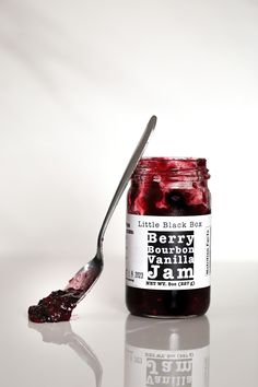 a spoon full of jelly sitting next to a jar of jam on a white surface