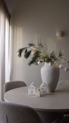 a white vase filled with greenery sitting on top of a table next to a window