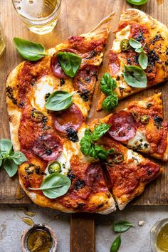 a pizza on a wooden cutting board with basil leaves and olives next to it