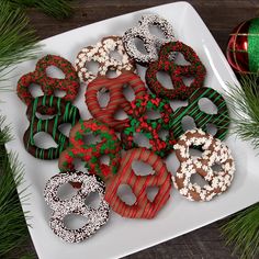 a white plate topped with lots of decorated donuts next to christmas tree branches and ornaments