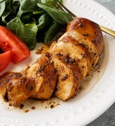 a white plate topped with chicken, tomatoes and spinach leaves next to a salad