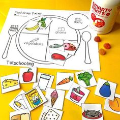 a table topped with lots of cut outs and food items next to a cup of yogurt