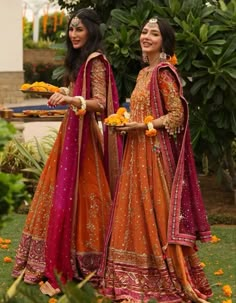 two women dressed in orange and pink outfits standing next to each other on the grass