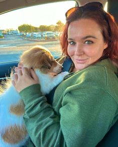 a woman sitting in the back seat of a car holding a puppy