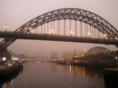 a bridge that is over some water with buildings in the background and lights on it