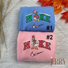 two different colored nike shirts sitting on top of a white fur covered floor next to autumn leaves