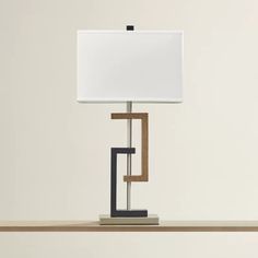 a table lamp with a white shade on it and a wooden shelf underneath the lamp