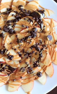 a white plate topped with sliced apple slices covered in chocolate chips and caramel sauce