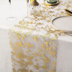 a table topped with a white and gold table cloth next to two wine glasses filled with yellow flowers