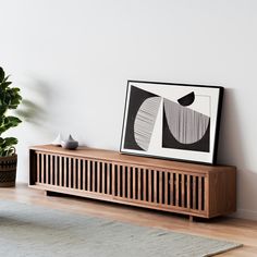 a wooden entertainment center with art on the wall and potted plant next to it