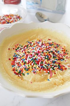 a bowl filled with batter and sprinkles on top of a white table