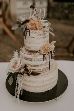 a three tiered wedding cake with flowers and leaves on the top is sitting on a table