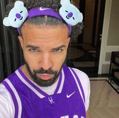 a man with two teddy bears on his head wearing a purple jersey and holding a basketball